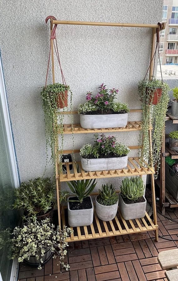 Bamboo garden shelf with hanging plant hooks on a balcony filled with various potted plants.