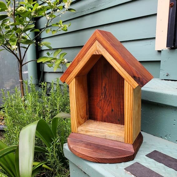 Birdhouse-style garden shelf mounted on a wooden fence.
