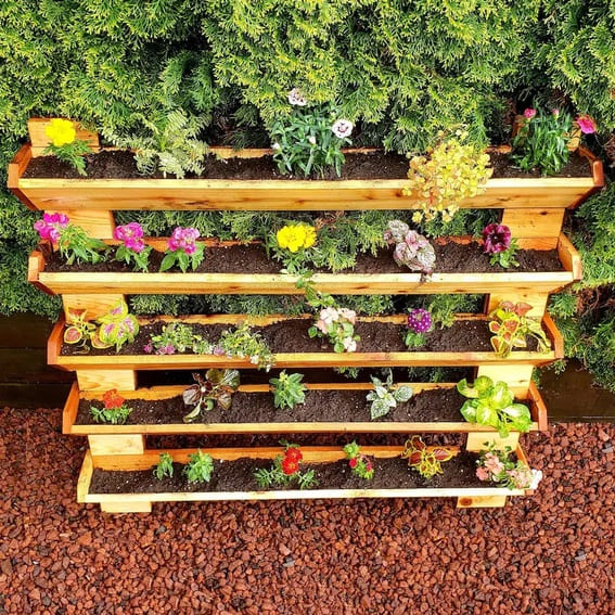 Five-tier wooden outdoor garden shelf with a variety of colorful flowers.