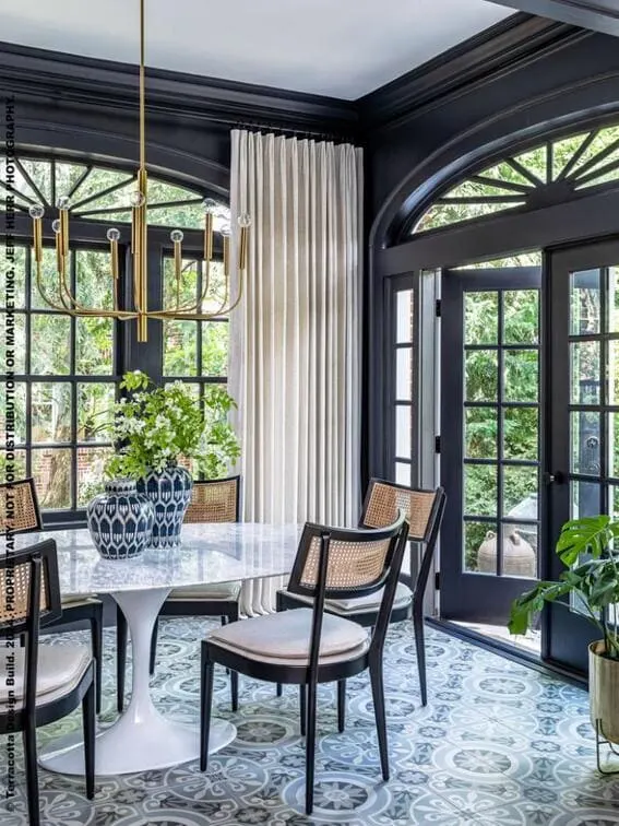 An inviting sunroom with deep blue trim, ornate flooring, and a statement lighting piece above sleek furniture.