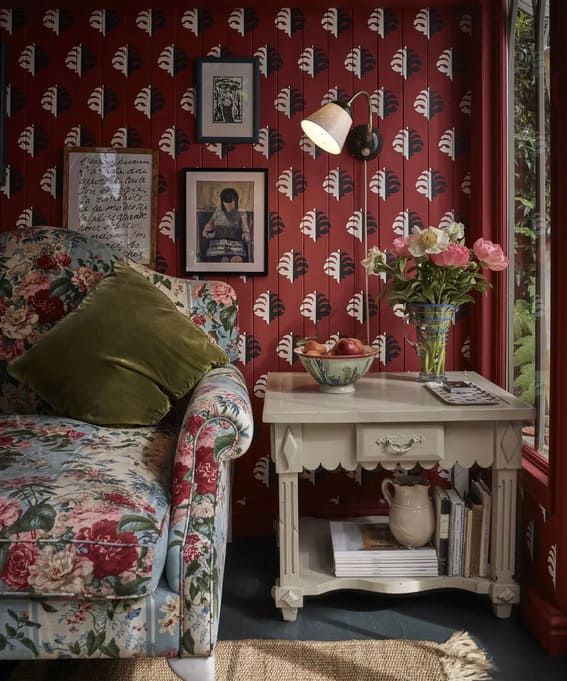 Vintage Red Floral Corner: A cozy, intimate corner with red wallpaper adorned with arch motifs, complemented by a floral-patterned armchair. The space is styled with vintage accents such as framed artwork, a wall-mounted lamp, and a white wooden side table with a vintage jug and books, creating a warm, nostalgic vibe.