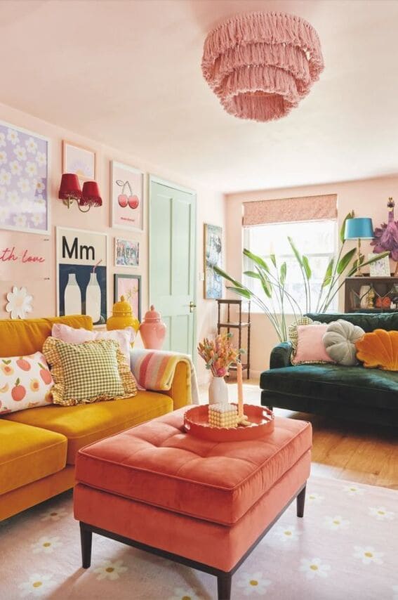  A colorful and eclectic living room featuring pastel pink walls, a pink fringed ceiling light, mustard yellow and green sofas, and a coral ottoman. Decor includes playful wall art and bold accessories.