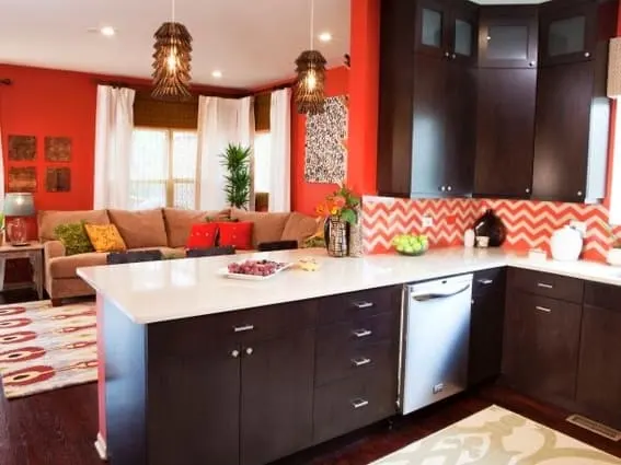 Open kitchen with orange walls and chevron backsplash connecting to a cozy living area.