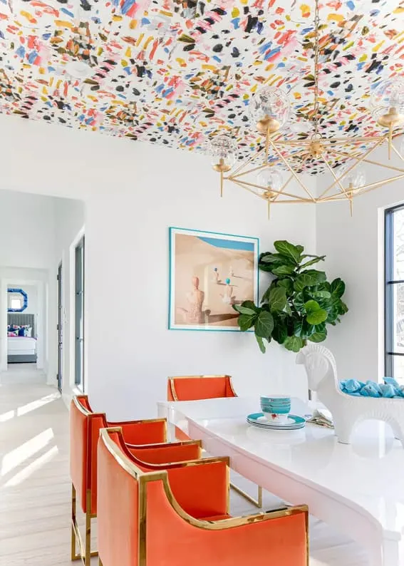 Sleek kitchen with orange and gold chairs under a colorful painted ceiling.