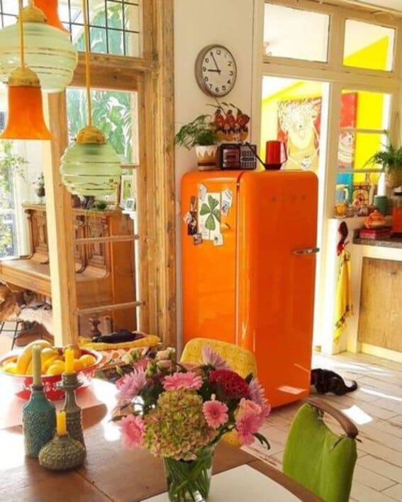 Sunny kitchen with a standout orange Smeg refrigerator, surrounded by colorful decor.