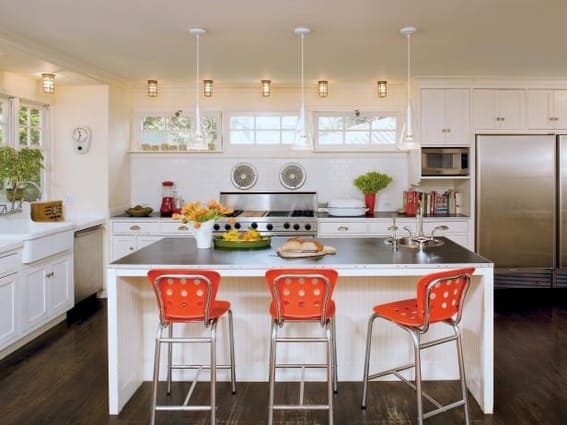 Bright kitchen with orange chairs at a white island and linoleum countertops.