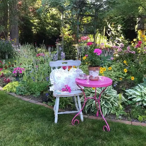 Cottage garden scene with pink bistro table, vintage chair, and blooming flower beds