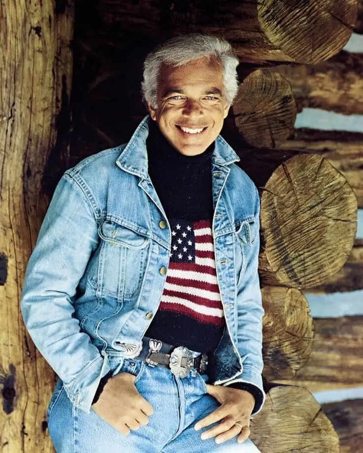 Denim-on-denim with an American-flag sweater at a rustic log cabin—classic Americana holiday style.