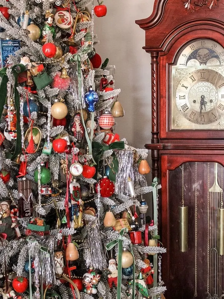 Vintage Christmas tree packed with nostalgic ornaments, silver tinsel, red apples and pears, beside a mahogany grandfather clock—Ralph Lauren holiday vibe.