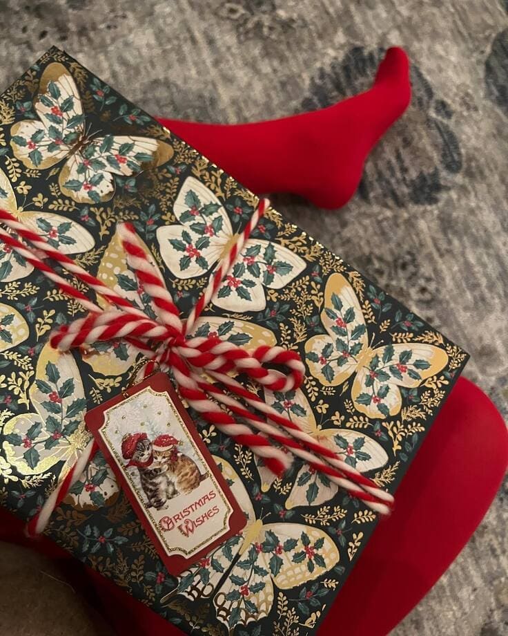 Butterfly holly gift wrap with candy-cane twine and vintage “Christmas Wishes” cat tag on red tights—Ralph Lauren holiday vibe.
