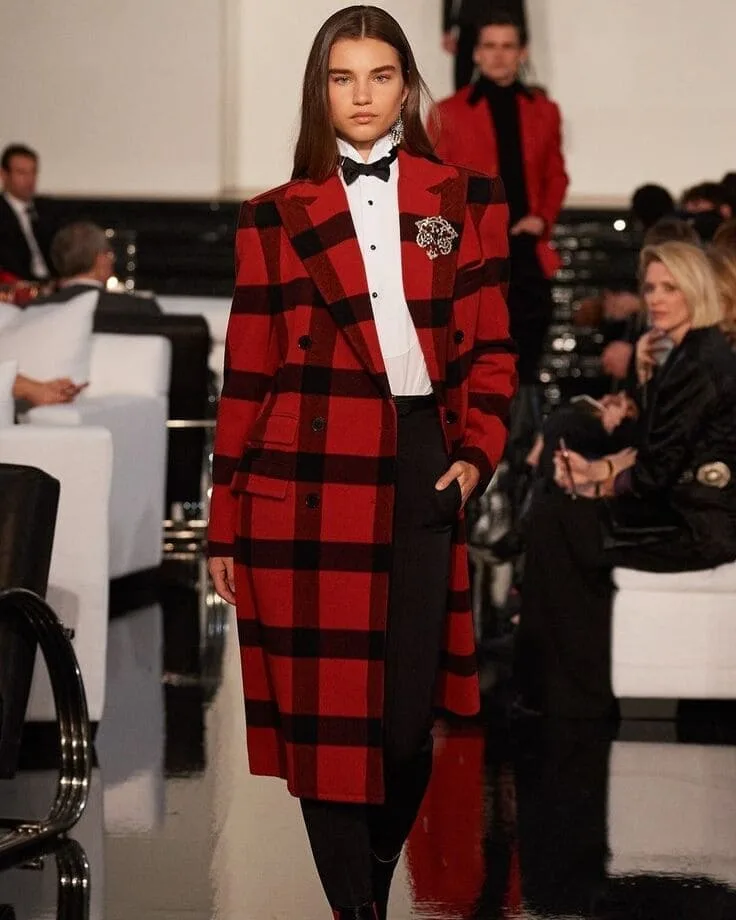 Ralph Lauren runway—red buffalo-check coat over tuxedo shirt and bow tie, jeweled brooch, black trousers.