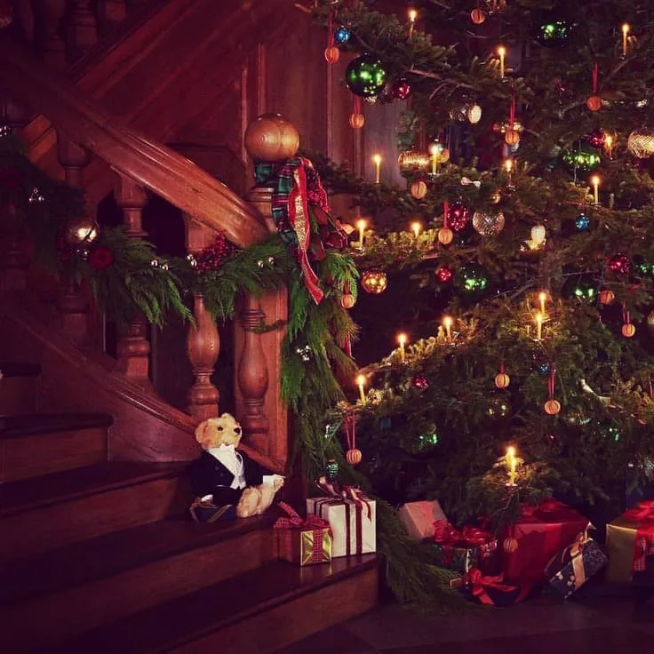 Ralph Lauren Christmas staircase—cedar garland with plaid ribbon, tuxedo Polo Bear on the steps, tree with clip-on candle lights and classic ornaments, tartan-wrapped gifts.