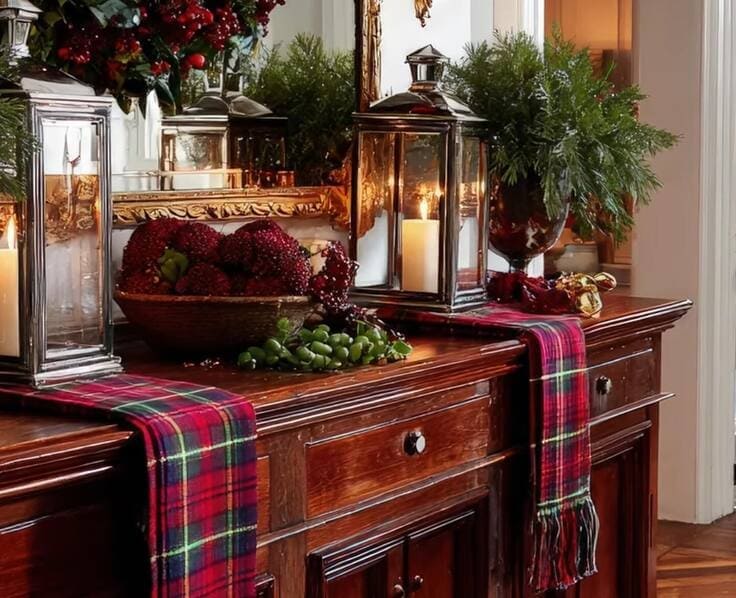 Ralph Lauren Christmas sideboard—mahogany buffet with tartan runners, silver lanterns with candles, bowl of pomegranates and grapes, fresh greenery, gilded mirror.