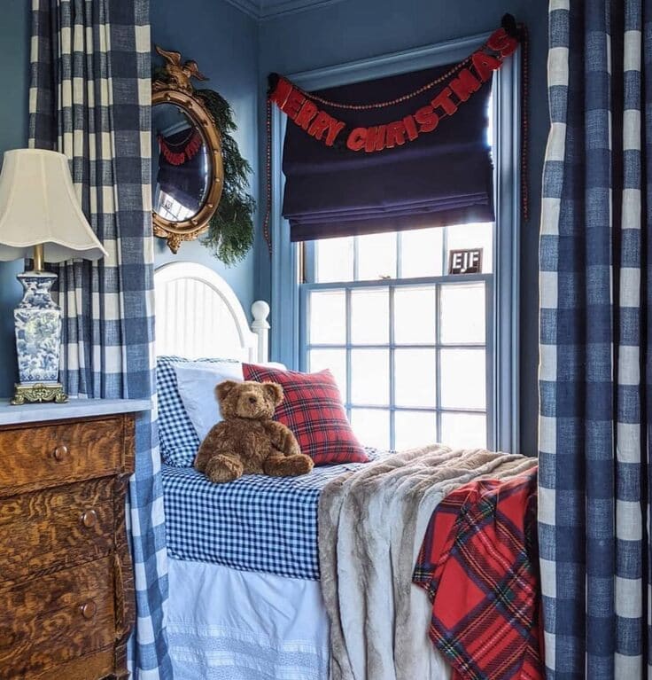 Ralph Lauren Christmas kid’s bedroom—buffalo-check drapes, navy gingham bedding, tartan blanket, teddy bear, blue walls, “Merry Christmas” banner.