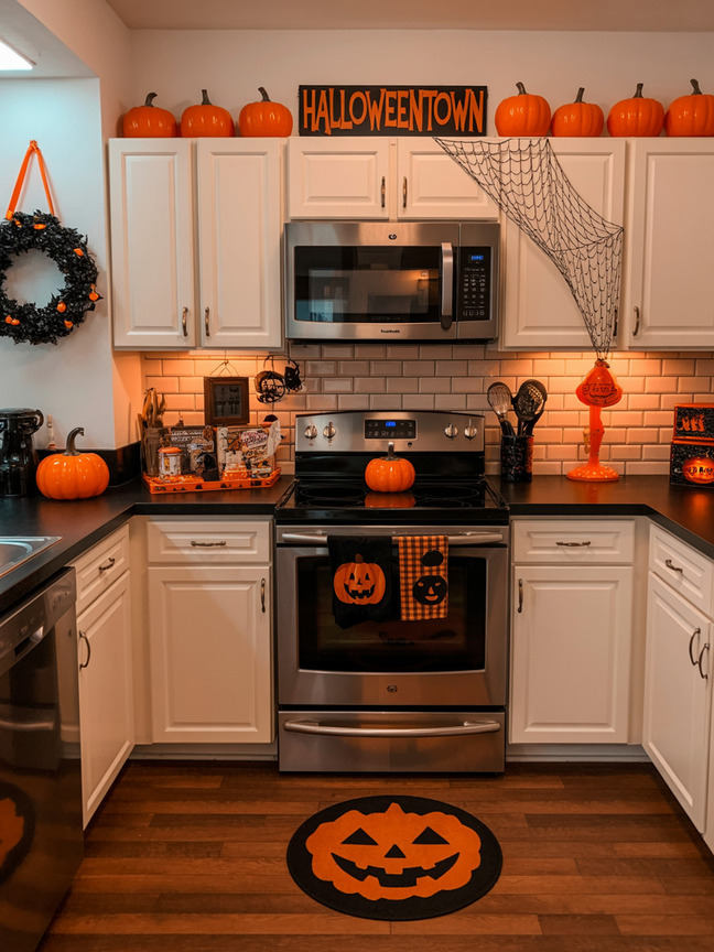 White kitchen decorated for Halloween with pumpkins, spiderweb decor, and orange accents