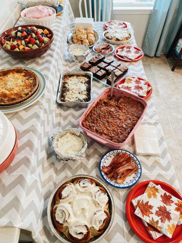 Friendsgiving potluck table with casseroles, cinnamon rolls, brownies and fruit
