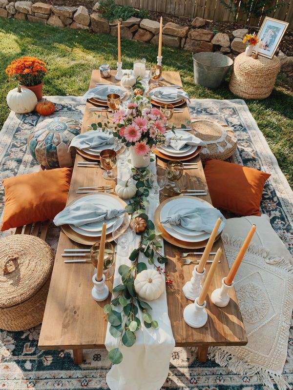 Outdoor Friendsgiving picnic table with fall decor and floor cushions