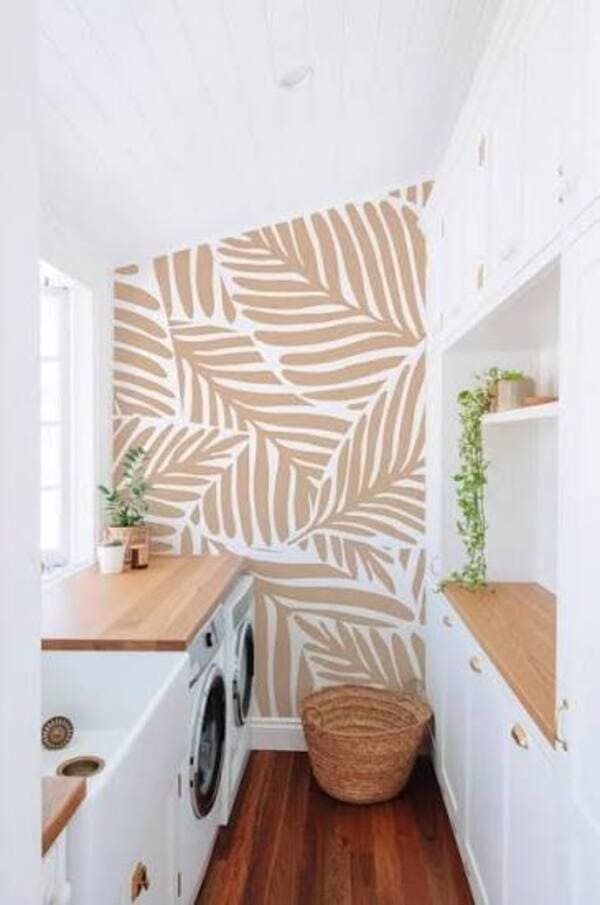 Narrow white laundry room with a washer under a wood counter, built-in storage and a beige leaf-pattern accent wall.