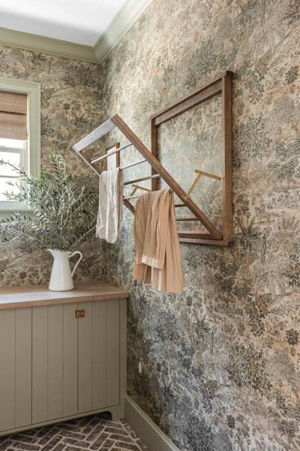 Wallpapered laundry room with a wall-mounted wooden drying rack holding clothes.