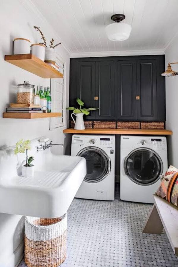 White laundry room with side-by-side washer and dryer, a utility sink, black upper cabinets and wood shelves.