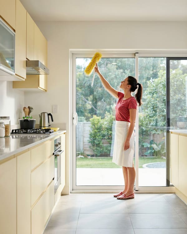 Woman dusting a high surface in a kitchen.