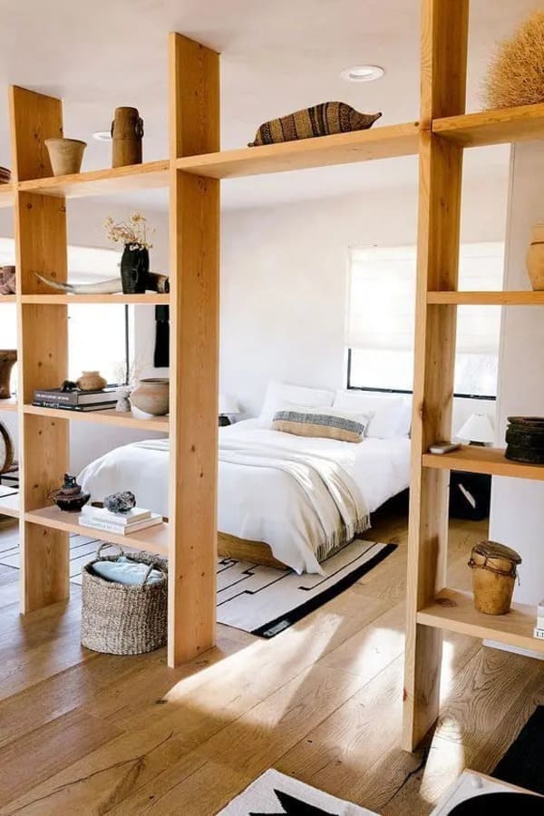 Open shelving divider separating a studio apartment bed from the living area