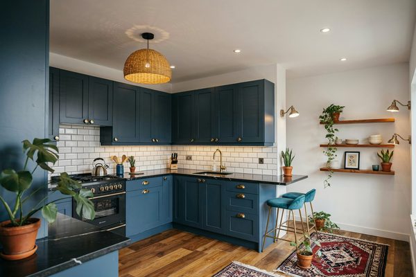Compact blue kitchen with brass hardware, breakfast bar, open shelves and plants